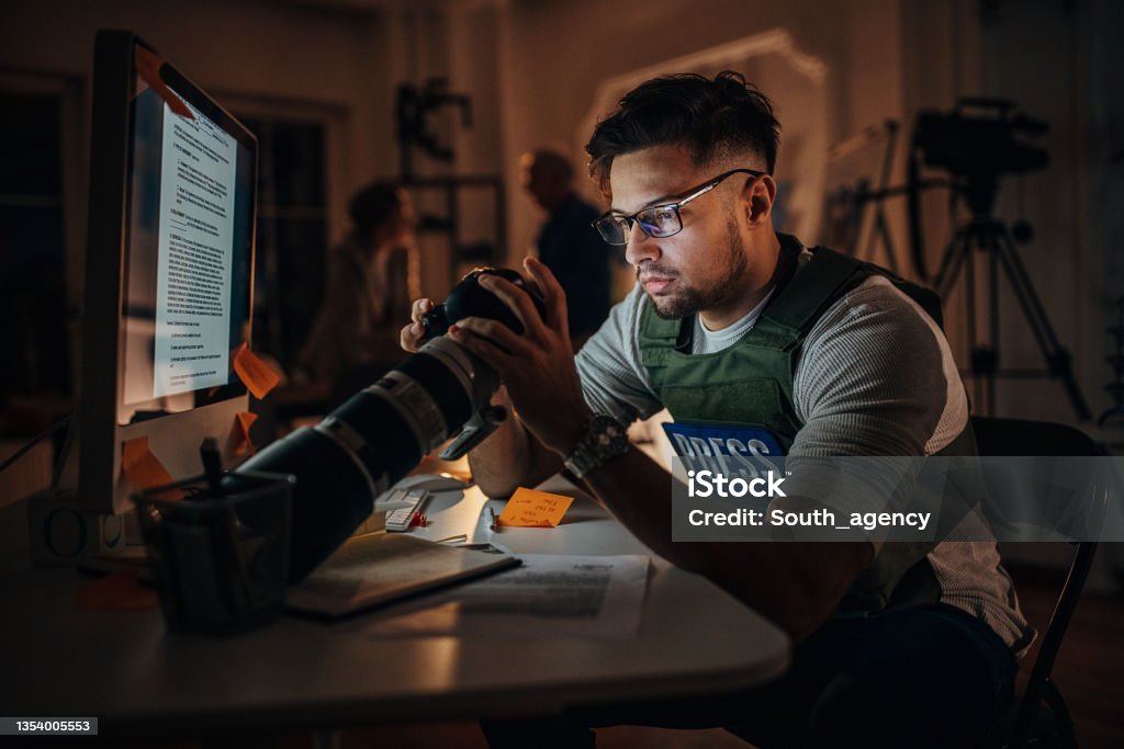 Photographer in news editorial office Three people, male photographer working at his desk in news editorial office at night. Reportage Stock Photo