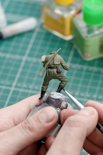 Scale Modeling. A man painting shoes on a plastic model of a soldier close up. WWII soldier figure 1:35. Hobby and leisure at home. Copy space