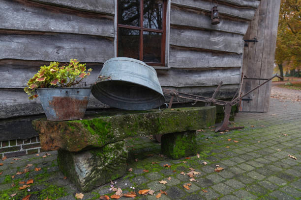 old zinc tub with old agricultural tools in a yard on a bench made of stones overgrown with moss