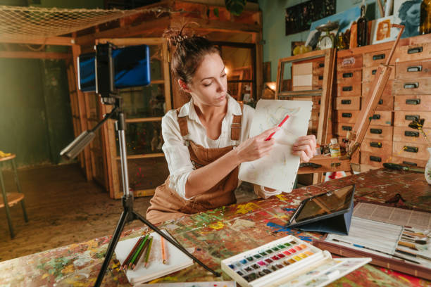 istock Female artist blogger at art studio recording her drawing master class using smartphone 1354016748