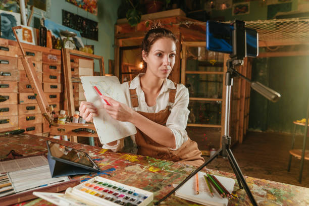 istock Female artist explaining drawing process recording livestream video at her workshop 1354016916