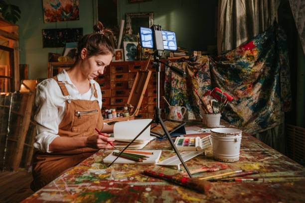 istock Caucasian young woman vlogger recording her illustration process using smartphone on tripod 1354017517