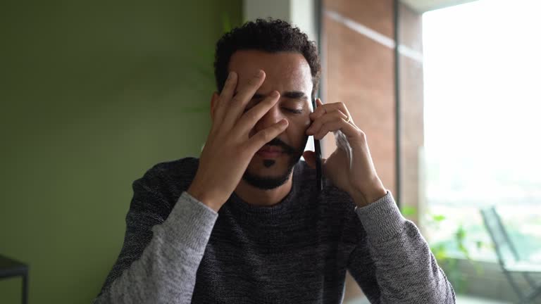 Worried man talking on the phone and using laptop at home