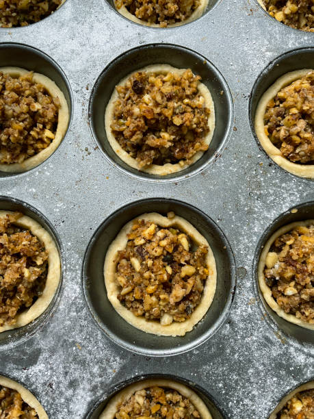 imagem completa da assadeira de muffin de tortas de menta individuais cruas, caseiras individuais, sobremesa de natal festiva massa de crosta de natal com carne doce (mistura de frutas secas picadas, espíritos destilados e especiarias) coberto com crumble - mince pie crumb christmas food - fotografias e filmes do acervo