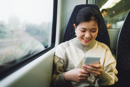 Smiling Asian young woman traveling by train and using smart phone