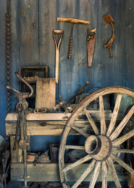 Wooden wagon wheel in repair shop Old wooden wagon wheel leaning against work bench in blacksmith shop wagon wheel bench stock pictures, royalty-free photos & images