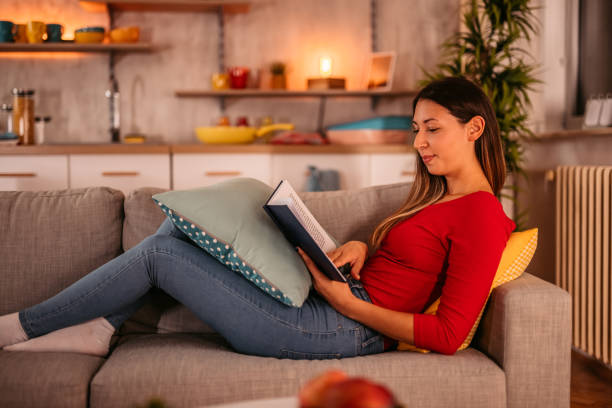 istock Woman lying on sofa at home and reading book 1354030108