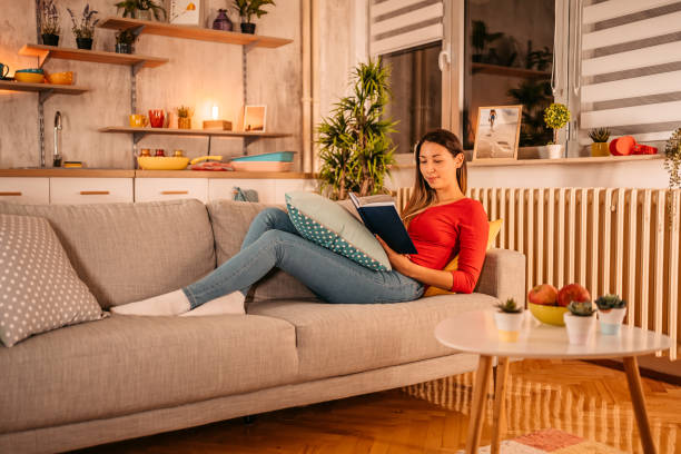 istock Woman lying on sofa at home and reading book 1354030150