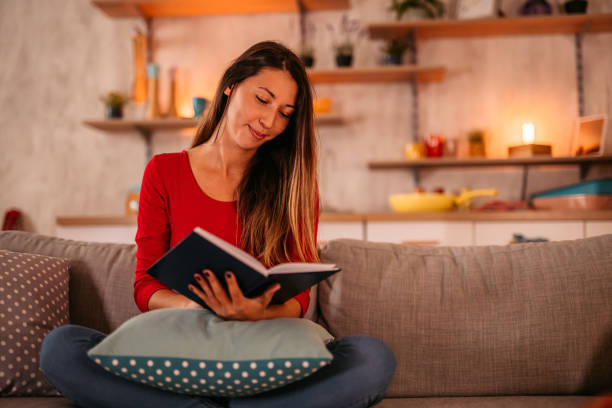 istock Woman lying on sofa at home and reading book 1354030253