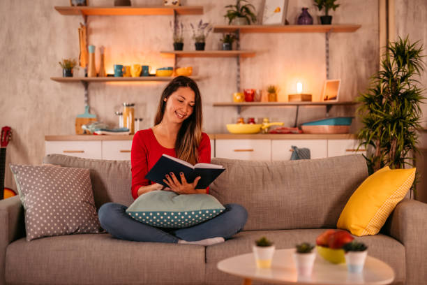 istock Woman lying on sofa at home and reading book 1354030343