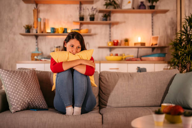 Sad woman sitting on sofa embracing pillow Woman looking depressed while sitting on sofa in living room and embracing pillow. curled up photos stock pictures, royalty-free photos & images