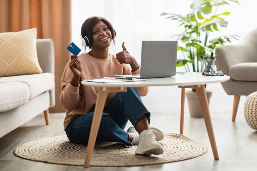I Like Online Shopping. African American Woman Showing Credit Card Gesturing Thumbs Up Using Laptop For Payment Sitting At Home, Smiling To Camera. Female Approving Bank Services