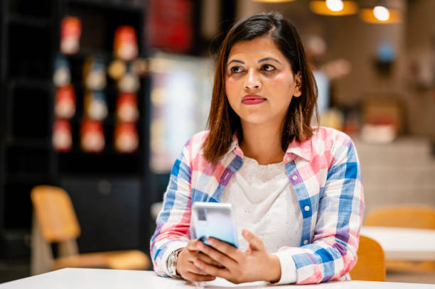 istock Young woman checking mobile phone while sitting at cafe. 1354035261
