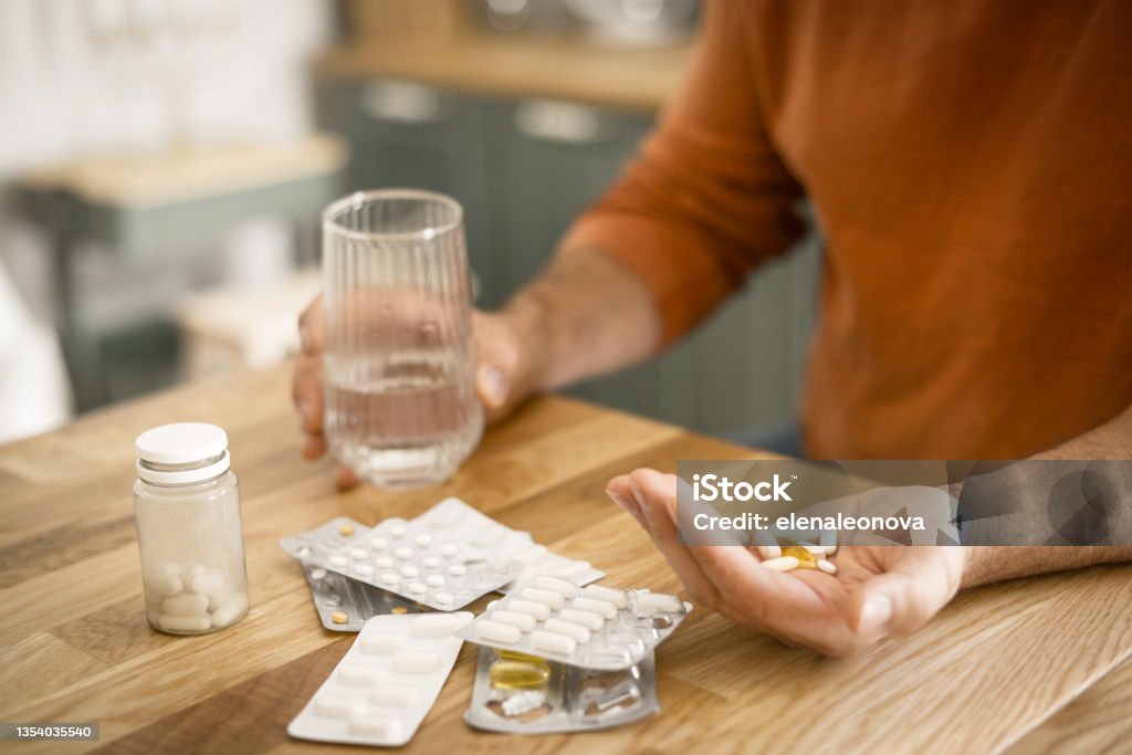 Mature adult man in cozy interior of home kitchen ( taking medication) Mature adult man in cozy interior of home kitchen Pill Stock Photo