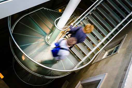 High angle image depicting an abstract view of two people running on a modern spiral staircase in the city. The running is depicted as motion blur, which makes it looks as though the person (we cannot tell if it is a man or a woman) is moving extremely fast. Room for copy space. ***IMAGE SHOT IN CITY HALL, LONDON, UK, A PUBLICLY OWNED BUILDING FREELY ACCESSIBLE TO THE PUBLIC. PLEASE NOTE THERE NO FEES OR TICKETS ARE REQUIRED TO ENTER, AND THERE ARE NO PHOTOGRAPHIC RESTRICTIONS***