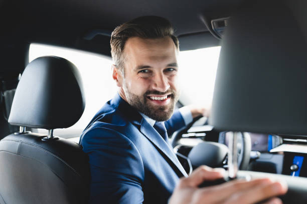 taxista sorrindo enquanto virava para o banco de trás olhando conversando com clientes. marido empresário bem sucedido olhando para o banco de trás na loja de revendedores antes de comprar um carro - back to front fotos - fotografias e filmes do acervo