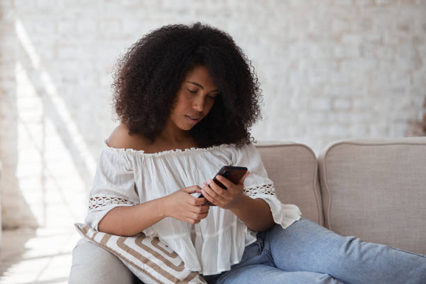 istock Thoughtful young mixed race woman freelancer brunette using smartphone sitting sofa. 1354037902