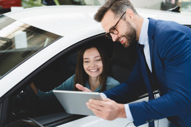 maschio bel commesso caucasico che mostra spiegando a un cliente femminile le opzioni di auto informazioni sul tablet digitale prima di acquistare la scelta di una nuova auto auto - ipad shopping gift retail foto e immagini stock