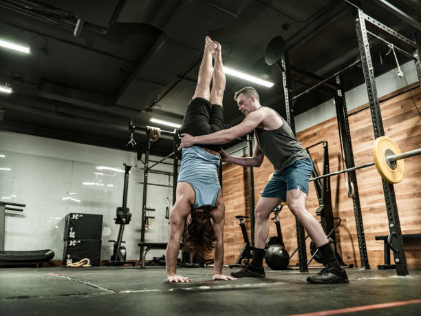 istock Young Man doing handstand with his trainer in the Gym 1354047309