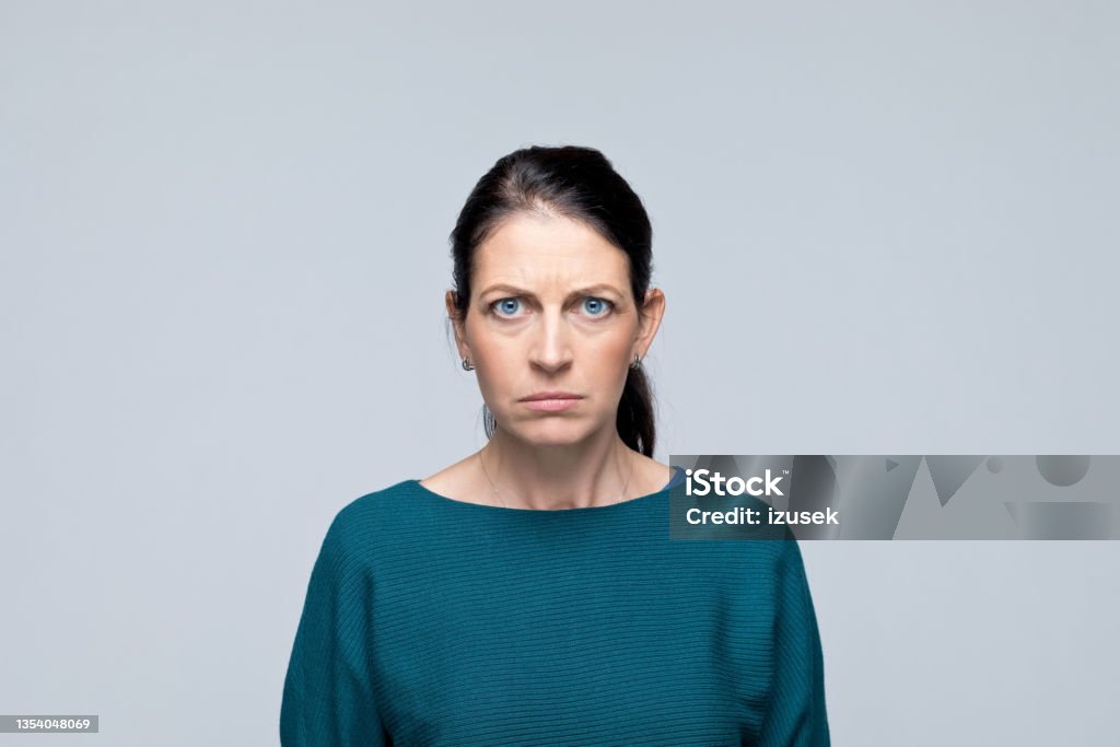 Headshot of angry mature woman Portrait of bossy mature woman staring at camera. Studio shot of female entrepreneur against grey background. Anger Stock Photo