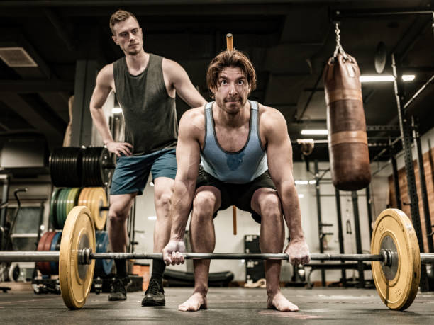 istock Young Man lifting weights with his trainer in the Gym 1354048409