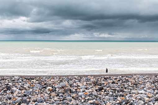 Alone in the world in the vastness of pebbles beach. Atlantic Ocean with a stormy weather in Hauts de France.  Mers-les-Bains in France. November 13, 2021.