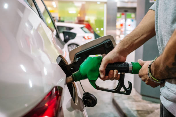 unrecognizable male putting fuel dispenser in tank while refueling vehicle on self service gas station - petrol imagens e fotografias de stock