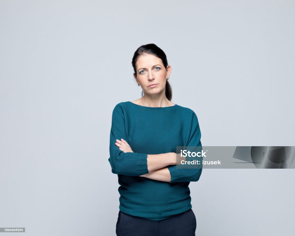 Portrait of displeased mature woman Portrait of sad mature woman standing with arms crossed and looking at camera. Studio shot of female entrepreneur against grey background. Women Stock Photo