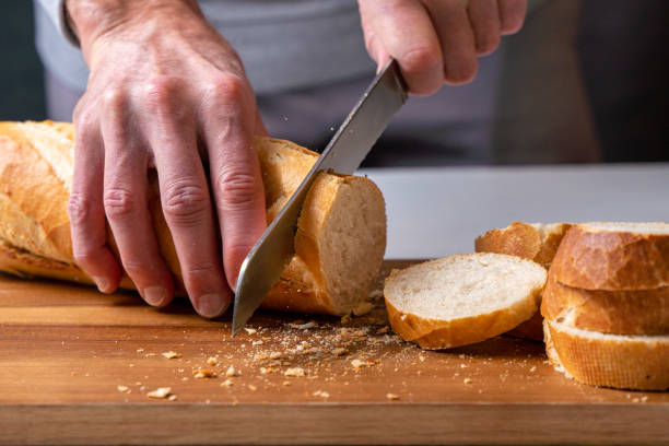 istock hands cutting a freshly baked baguette into slices on a wooden board, front view. 1354050621