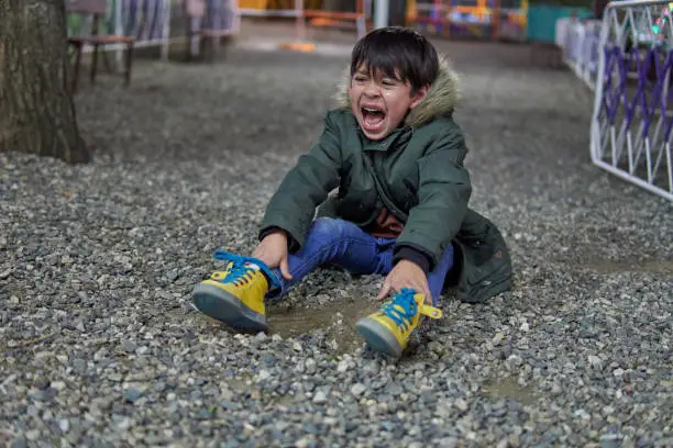 Photo of sad and upset child latin boy shouting and crying sitting on the pebble floor in a amusement park. concept for caprice, depression stress or frustration. Horizontal