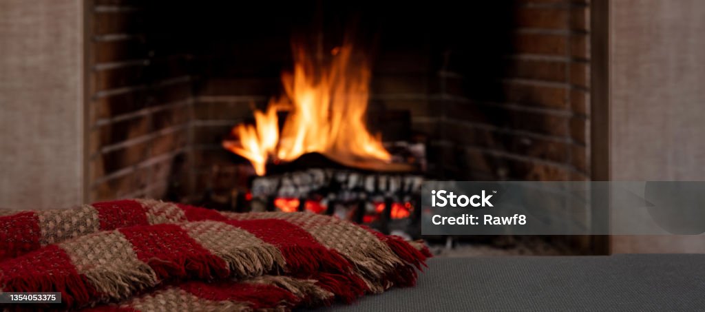 Blanket on fireplace burning wood logs background. Relaxation and Christmas holiday, cozy warm home Relaxation near the fire, Christmas holiday cozy warm home interior. Blanket on the sofa, fireplace burning wood logs background. Cozy Stock Photo