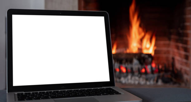 istock Christmas winter home office concept. Blank screen laptop on burning fireplace background, 1354053378