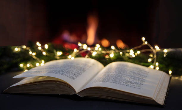 istock Christmas reading and relaxing by the fire, Book open, xmas tree lights, fireplace burning 1354053396