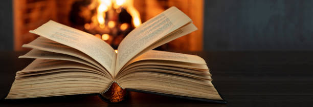 istock Book open, fireplace burning firewood background. Reading and relax near the fire 1354053410