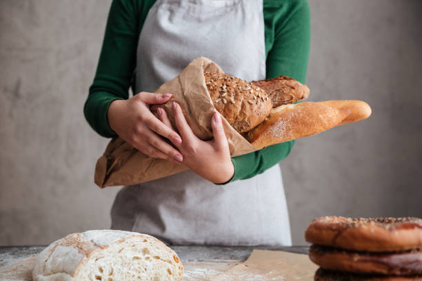 istock Cropped image of  female baker holding bag with bread 1354059589