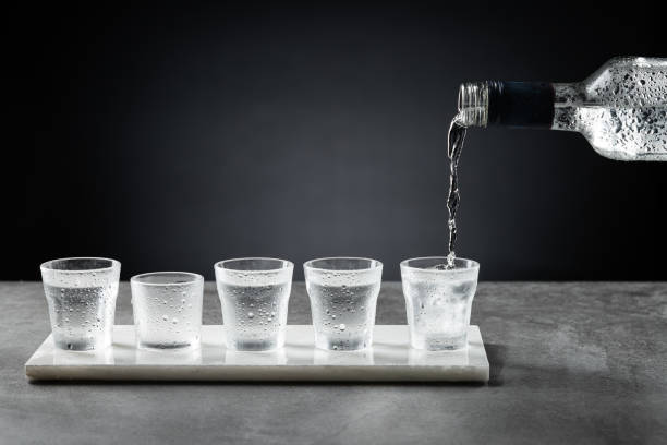 verser de la vodka froide dans du verre à shot isolé sur fond sombre. mise au point sélective. - liqueur photos et images de collection
