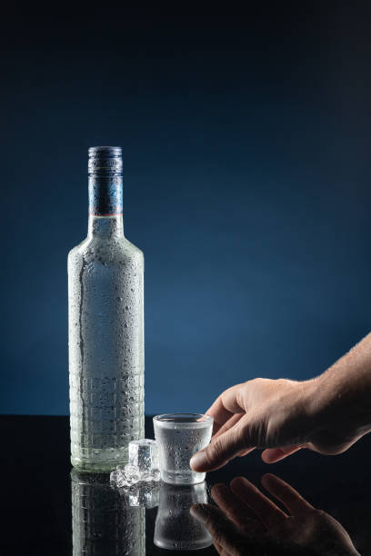 mano che prende un bicchierino di vodka su sfondo blu scuro. formato verticale. copia spazio. - martini brand vermouth foto e immagini stock