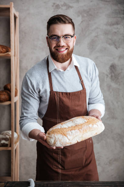 istock Cheerful young man baker standing at bakery holding bread 1354060775