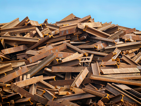 A stack of rusty old sections of railway track in a scrap metal yard.