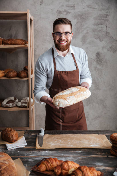 istock Cheerful young man baker standing at bakery holding bread 1354060943