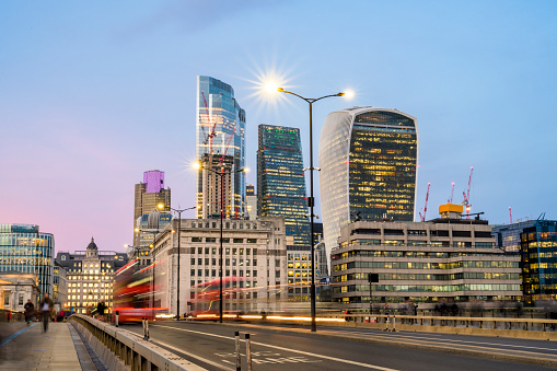 City of London skyline with red bus and illuminated street lamps at blue hour