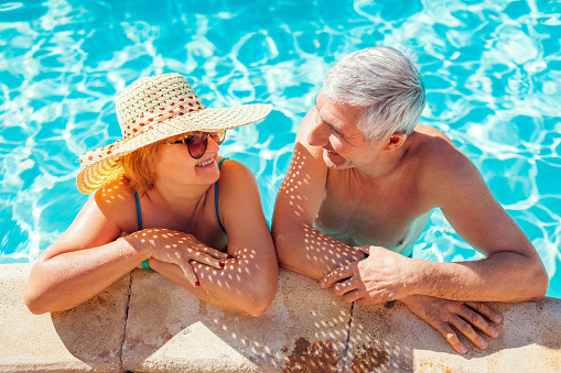Senior retired family couple relaxing in resort swimming pool. Happy people enjoying summer vacation in tropical exotic hotel. All inclusive.