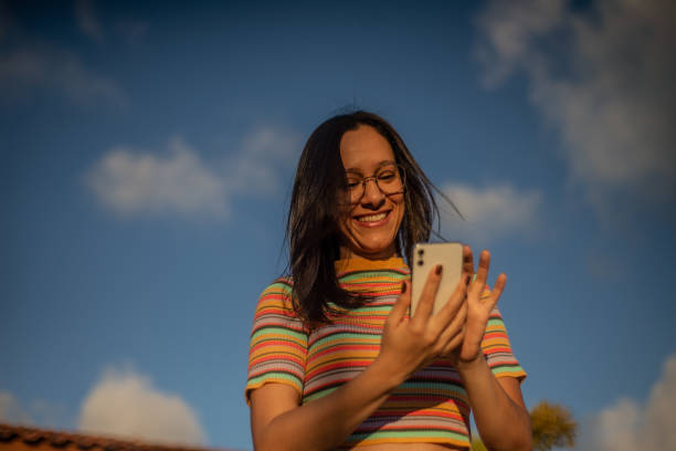 istock Young woman using smart phone. Blue sky. Eyeglasses 1354062738