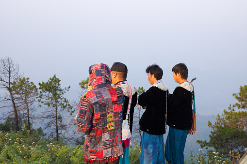 Four rhai men are looking into landscape on top of mountain Doi Mong Angkhet in Chiang Mai province. in morning. Rear side view of men. Three are wearing traditional local fashion