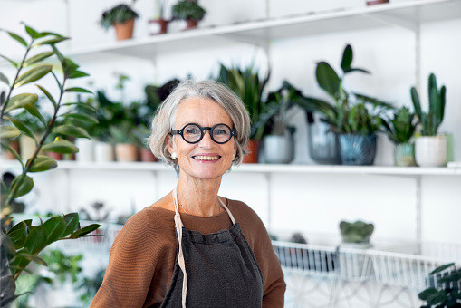 Portrait of senior female florist at small business flower shop. Happy mature woman wearing apron working in a small flower store.
