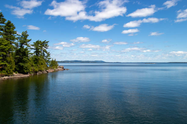 view of a tree lined coast and calm water and blue sky in the North Channel on The Great Loop in Canada