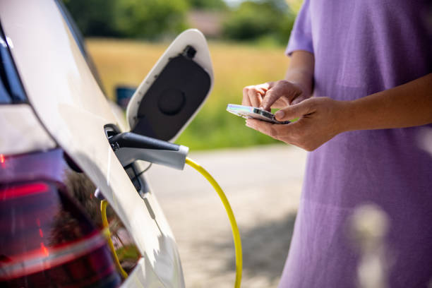 istock Woman using mobile phone while charging electric car 1354069665