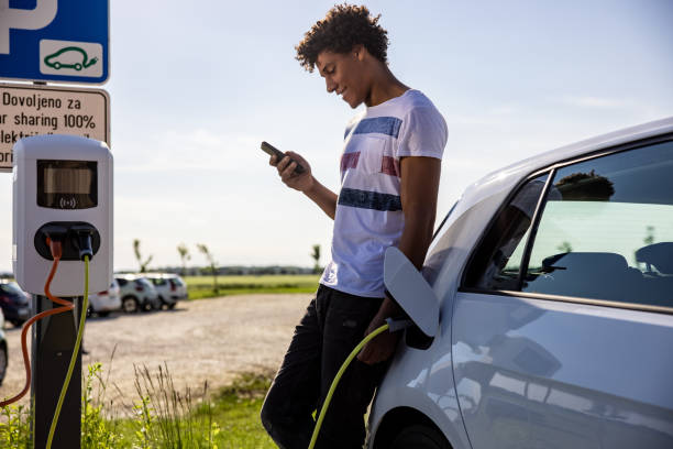 istock Man using mobile phone while charging electric car outdoors 1354069875