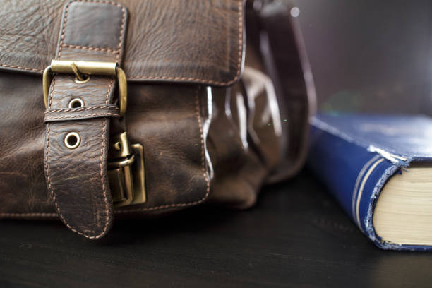 istock Old leather briefcase with metal buckles and a closed book lying on the table. Education concept. 1354069908