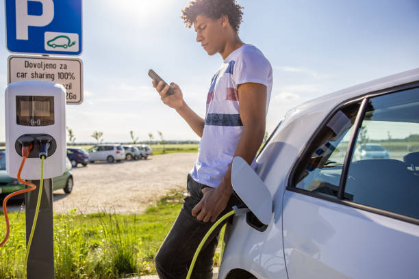 istock Man using mobile phone while charging electric car outdoors 1354069918